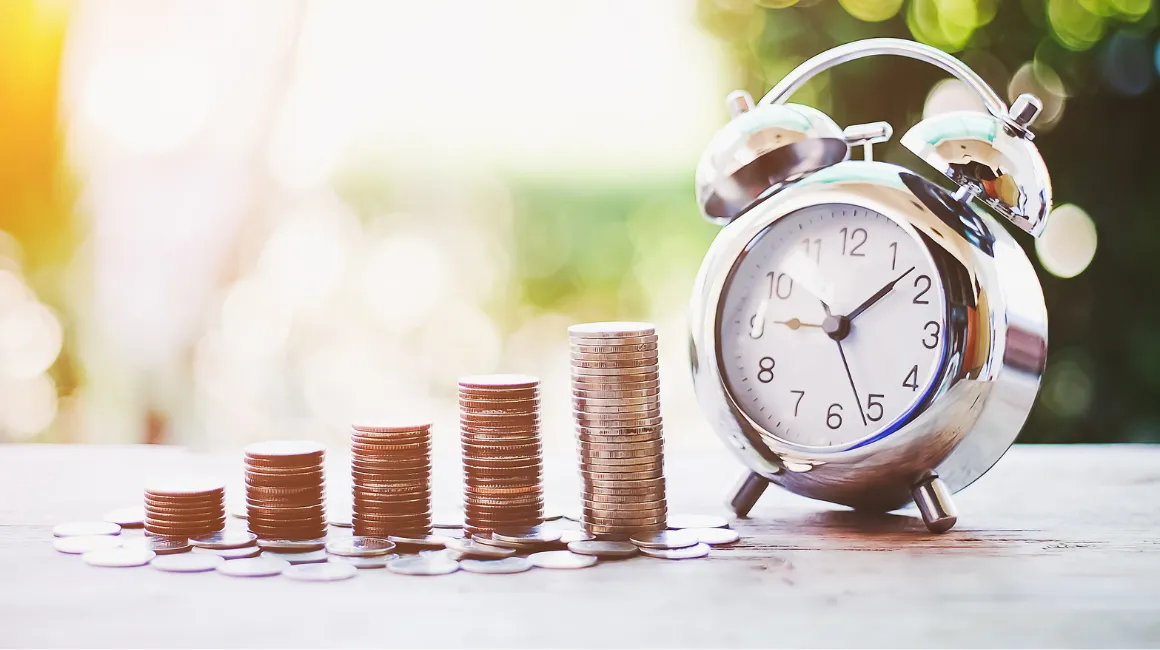 rosnące stosy monet obok klasycznego budzika